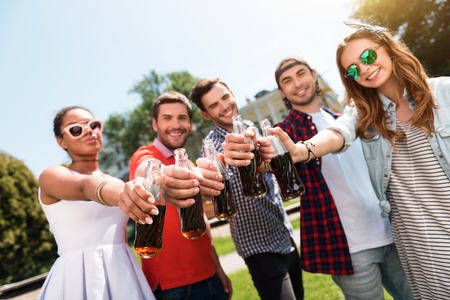 Celebrate your life. Positive and cheerful group of young people holding cola bottles together while being in the park and spending nice timeの写真素材