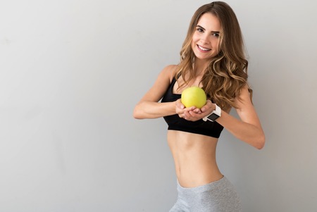 My remedy. Positive charming young woman holding an apple and smiling while feeling contentの写真素材