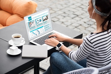 Nice weekend. Pleasant young woman sitting at the table and reading news while using laptop