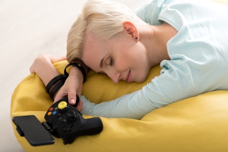 After keeping late hours. Tired woman sleeping on the bean bag with a smartphone connected with gamepadの写真素材
