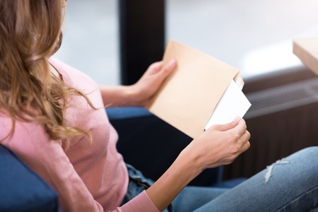 News from abroad. Pleasant young woman sitting on the couch and holding letter while opening itの写真素材