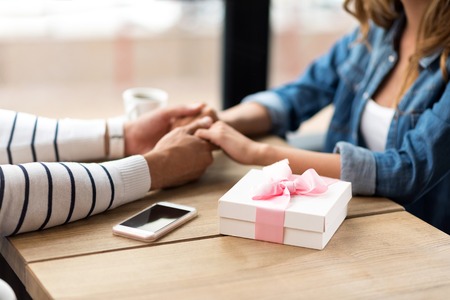 True feelings. Close up of hands of loving couple holding them together and sitting at the table while having a dateの写真素材