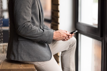 Always connected. Pleasant businessman sitting on the table and using cell phoneの写真素材