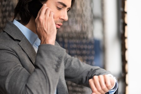 Call me back. Pleasant serious handsome man looking at his wrist watch and talking on cellphoneの写真素材