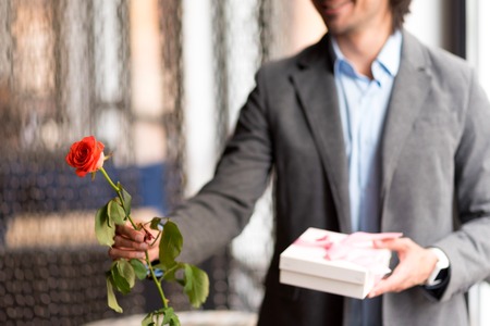For you my dear. Close up of rose in hand of pleasant cheerful man holding it and giving present while expressing joyの写真素材