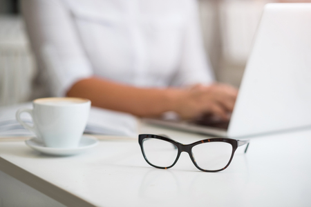 Working atmosphere. Selective focus of glasses ling on the table while pleasant senior woman sitting in the backgroundの写真素材