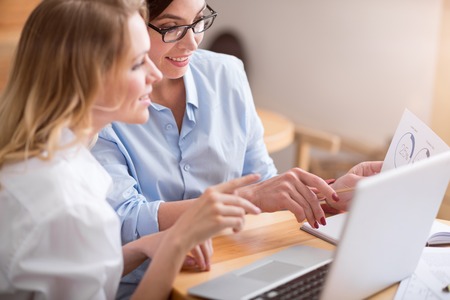 Gathered. Cropped image of content and cheerful business women using laptop while holding papers and working togetherの写真素材