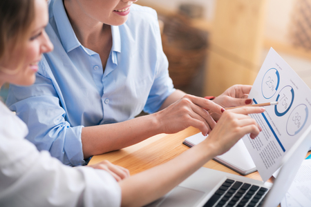 Best team. Cropped image of positive business women using laptop while holding papers and working togetherの写真素材