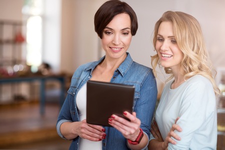 Tablet usage. Positive and happy young women holding and using digital tablet while communicatingの写真素材