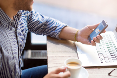 New message. Pleasant bearded man sitting at the table and using cell phone while drinking coffee