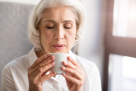 Nice taste. Pleasant delighted woman holding cup and drinking tea while resting in the cafeの写真素材
