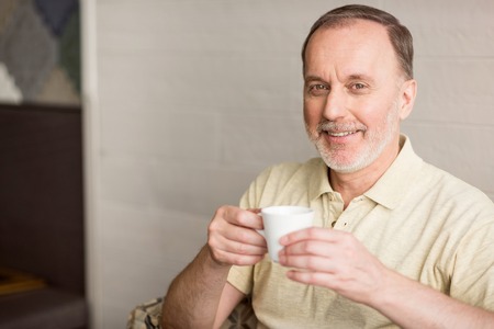 Time for relaxation. Positive delighted senior man smiling and drinking coffee while resting in the cafeの写真素材