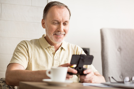 Best time to relax. Cheerful senior man sitting at the table and playing video games while expressing positivityの写真素材