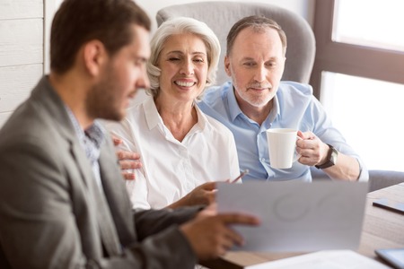 Ready for new bargain. Cheerful senior couple sitting at the table and listening to professional sales manager while expressing positivityの写真素材