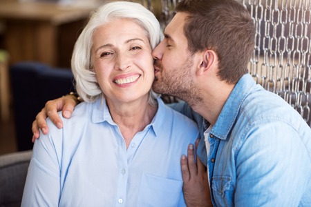 Love you so much. Joyful smiling senior woman expressing joy while her grandson kissing herの写真素材