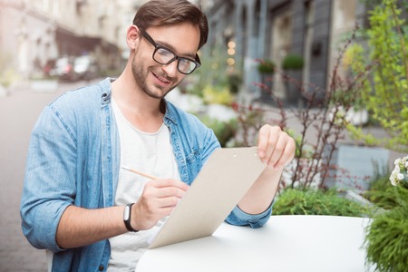 Creativity and imagination. Joyful bearded handsome man drawing a picture and smiling while sitting at the tableの写真素材