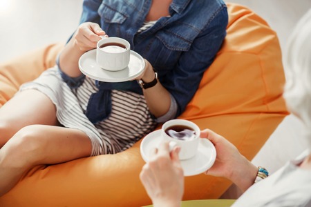 Refresh your mind. Top view of pleasant women sitting in the puffs and drinking coffee while restingの写真素材