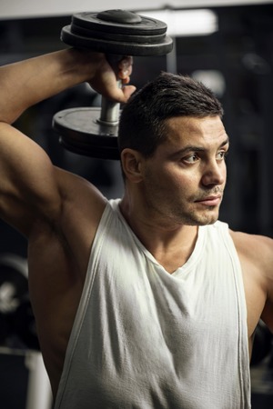 Strong and powerful. Handsome serious brunette man holding a dumbbell up and looking to the left...