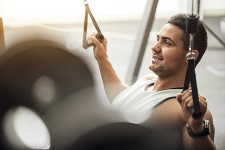 Pleasant workout. Delighted emotional young man doing a physical exercise and smiling while training