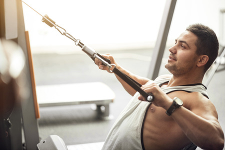 Build up your muscles. Good looking positive professional sportsman doing a physical exercise and smiling while taking pleasure in the workout.の写真素材
