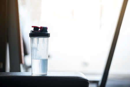 Drink me. Close up of a small half full bottle of mineral water standing on the gym apparatus near the windowの写真素材