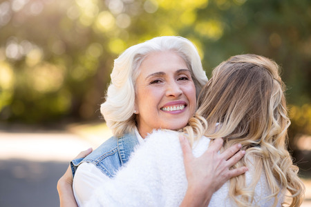 My little adult girl. Beautiful gray haired woman hugging her daughter and smiling while standing in the park.の写真素材