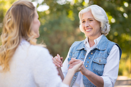 You make me smile. Pretty old woman smiling and holding hands of her daughter while having a walk in the park.の写真素材