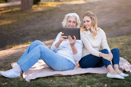 Happy time together. Beautiful charming mother and daughter sitting on the grass and smiling while...