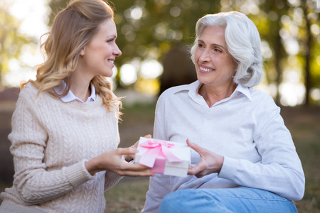 You make me happy. Pretty delighted mother and daughter smiling and sitting on the ground while holding present box.の写真素材