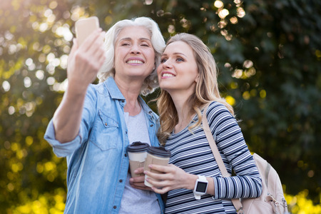 We are so beautiful. Satisfied pretty mother and daughter smiling and taking selfie while having a...