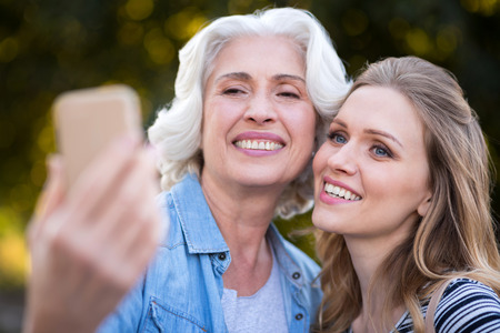 Pleasant moment. Beautiful charming mother and daughter smiling and taking selfie while walking on...