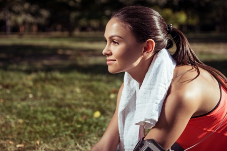 Beauty of sport. Smiling young beautiful active girl posing after having outdoors training while sitting in the park.の写真素材