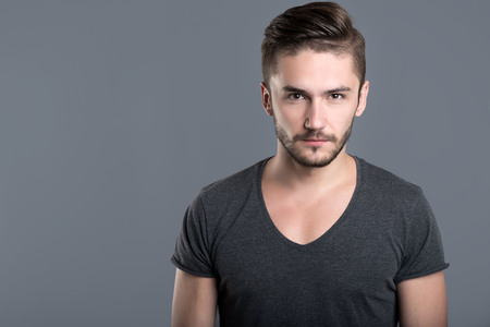 Feeling of anger. Annoyed bearded young man standing against grey backgroundの写真素材