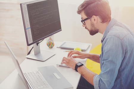 Without any mistake. Concentrated enthusiastic young programmer coding while using computer and...