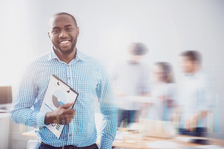 Ready to start. Handsome bearded guy smiling and holding folder with some infographcs on it in front of blurred effect and virtual screen.の写真素材