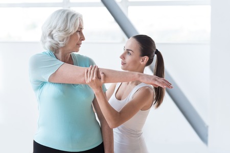At the fitness centre. Skillful experienced female coach standing near the woman and holding her hand while looking at herの写真素材