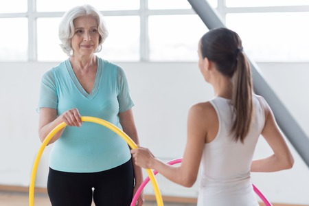 Having fitness workout. Happy energetic good looking women standing in the gym hall and holding  hoops while enjoying their fitness trainingの写真素材