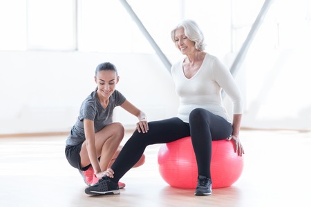 Pleasant people. Optimistic good looking nice woman stretching out her leg and smiling while sitting on a fitness ballの写真素材
