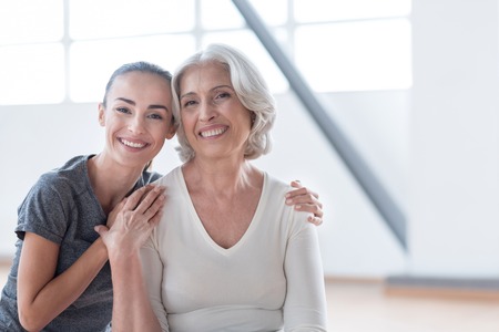 Joy and happiness. Good looking nice delighted women looking at you and smiling while sitting together in a fitness hallの写真素材
