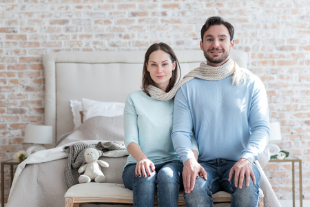 Happy together. Pleasant happy young couple sitting side by side and sharing a scarf while looking at youの写真素材
