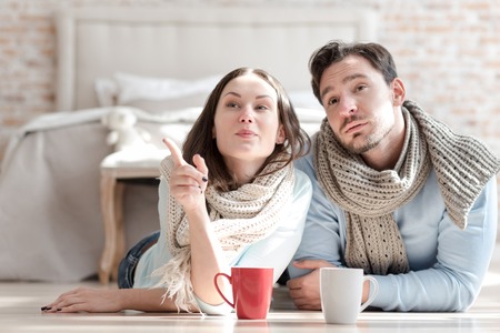 Look at this. Attractive elated young woman lying on the floor and pointing at something while showing it to her boyfriendの写真素材