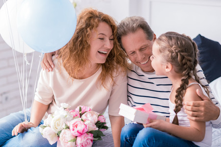 I love my caring grandparents. Happy little girl sitting on the bed with her grandparents and...