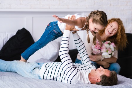 I enjoy flying. Delighted little girl playing games with her grandparents while lying on the bed and...