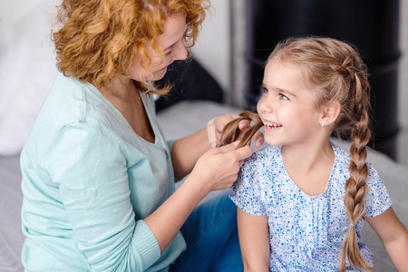 Happiness. Smiling grandmother plaiting braids to her little granddaughter while resting togetherの写真素材