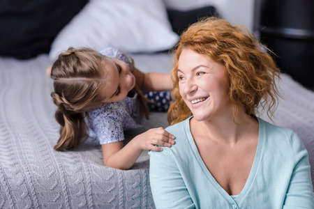 Merry weekend. Delighted little granddaughter having fun with her grandmother at home while smiling and resting togetherの写真素材