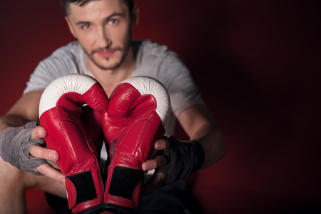 Take it. Top view of young handsome bearded man holding boxing gloves while sitting on floor.の写真素材