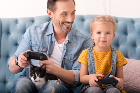 Having fun. Cheerful positive god looking father and his daughter holding a game console and playing...