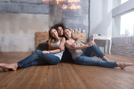We love each other. Positive delighted young girls smiling and hugging each other while sitting in the bedroom on the floor and expressing happinessの写真素材