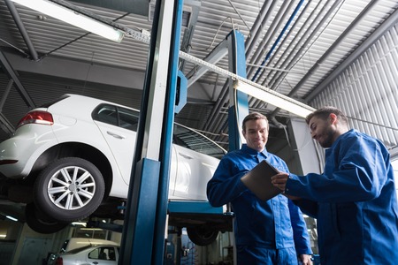 Low angle of positive delighted mechanics using tablet and going to repair car while working in auto serviceの写真素材