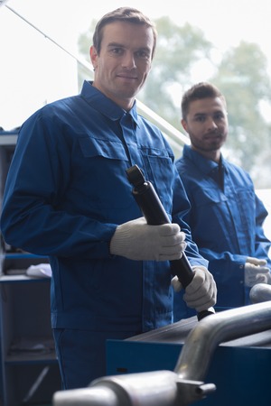 Professional delighted adult car mechanic holding tool and repairing car while working with his colleague in auto serviceの写真素材